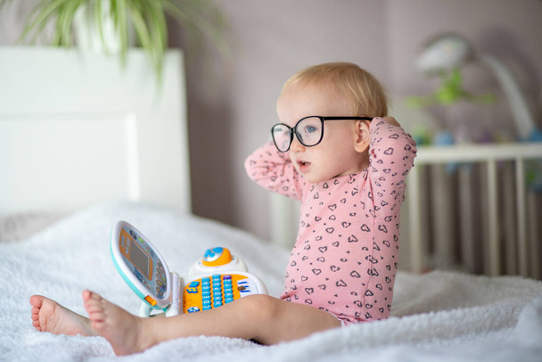 Cute toddler in glasses sitting on bed with a toy laptop - Photo, Image