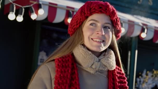 Winter season vibes. Christmas festive atmosphere. Happy girl waiting when her friends come to favorite cafe. Hiding neck with red knitted scarf. Woman in the winter town looking for taxi. High - Footage, Video