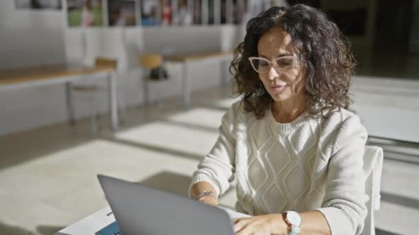 Érett spanyol nő laptopot használ modern irodai környezetben, gondolatot és koncentrációt fejez ki. - Felvétel, videó
