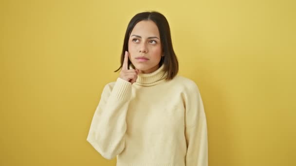Young beautiful hispanic woman wearing sweater standing pointing finger up with successful idea. exited and happy. number one. over isolated yellow background - Footage, Video
