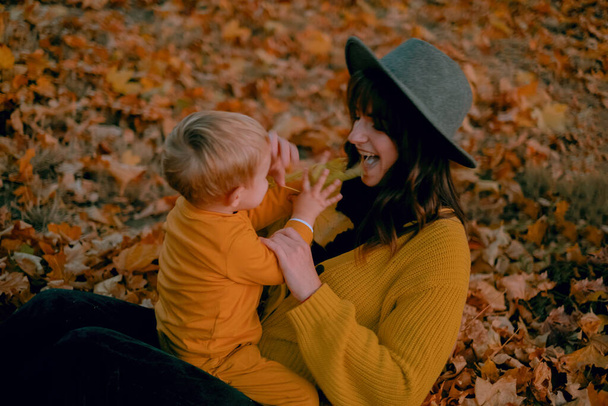 Une mère et son fils passent du bon temps ensemble, jouant dans le parc d'automne, tous deux vêtus de vêtements jaunes. Au milieu du feuillage coloré, ils partagent des moments joyeux, des rires résonnant dans l'air croustillant. - Photo, image
