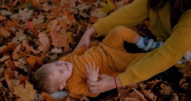 Bir anne ve oğlu birlikte güzel vakit geçirir, sonbahar parkında oynarlar, ikisi de sarı giyinir. Renkli yaprakların arasında, neşeli anları paylaşıyorlar, taze havada yankılanan kahkahalar.. - Fotoğraf, Görsel