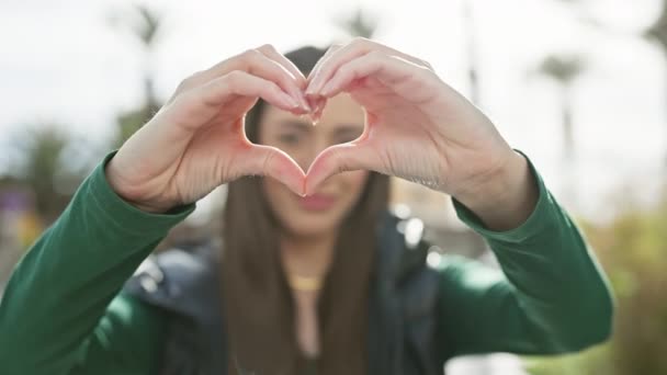 Smiling woman forming a heart shape with her hands outdoors in a casual setting - Footage, Video