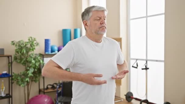 Starší muž procvičuje dechová cvičení ve fyzioterapeutickém prostředí - Záběry, video