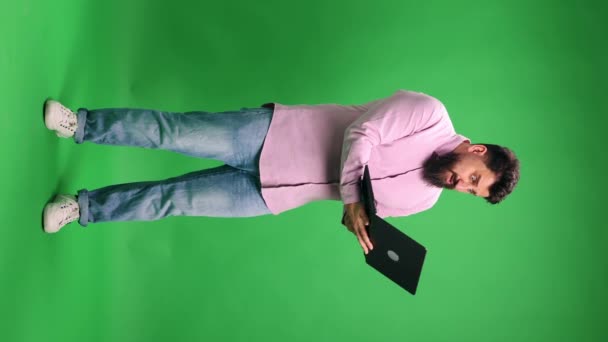 Mann in legerem Outfit öffnete Laptop und blickt überrascht auf Bildschirm vor leuchtend grünem Studiohintergrund. Konzept menschlicher Emotionen, Selbstausdruck, Arbeit und Studium online. Vertikale Orientierung - Filmmaterial, Video