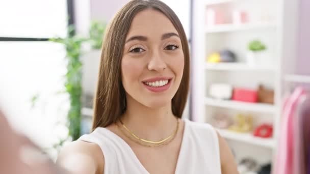 Hymyilevä nainen ottaa selfien kirkkaassa, sekavassa pukuhuoneessa, jossa on värikkäitä vaatteita ja asusteita.. - Materiaali, video