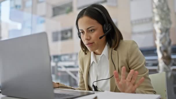 Jonge Spaanse vrouw met headset werken op laptop in modern kantoor met uitzicht op de stad. - Video