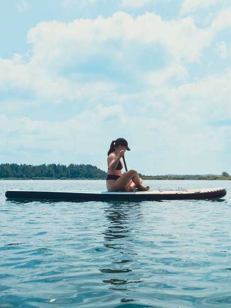 όμορφη γυναίκα κάθεται στο supboard κωπηλασία στη μέση της λίμνης - Φωτογραφία, εικόνα
