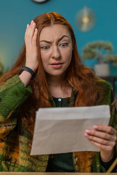 Erstaunt öffnet eine traurige Frau den Umschlag und liest schlechte Nachrichten in Briefen. Finanzprobleme, Bankschulden, Steuernachzahlungen oder Konkursanzeigen. Vertikal - Foto, Bild