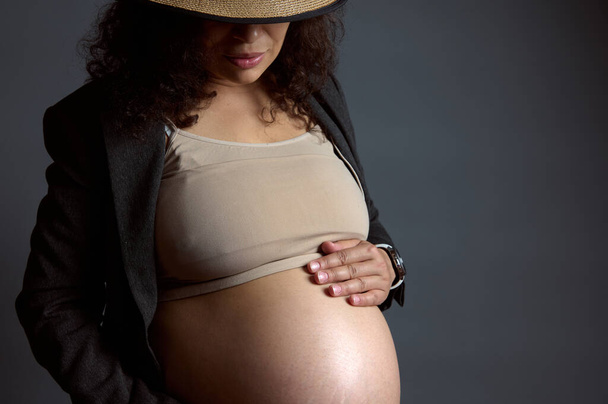 Detailní záběr portrét mladé krásné klidné těhotné ženy jemně hladí její břicho, těší její šťastný bezstarostné těhotenství, izolované přes módní šedé studio pozadí s volným reklamním prostorem - Fotografie, Obrázek