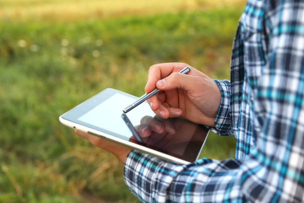 Een agronomist gebruikt een digitale tablet in een jong maïsveld bij zonsopgang of zonsondergang. Close-up van de handen met tabletscherm en stylus. - Foto, afbeelding