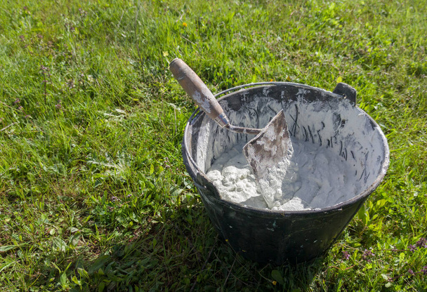Bucket full white adhesive mortar ready for applicate. Green grass as background - Photo, Image