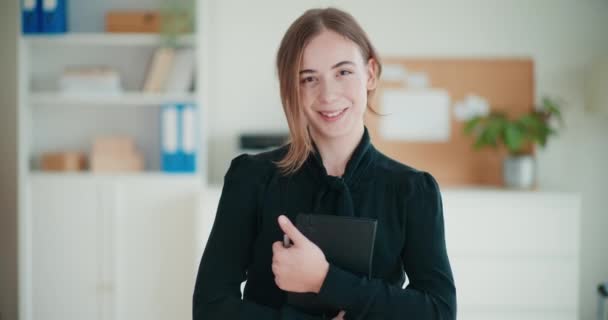 Portret van een lachende jonge zakenvrouw met dagboek en pen terwijl ze op kantoor staat - Video