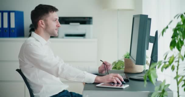 Gefrustreerde jonge zakenman met behulp van computer tijdens het zitten aan het bureau in het kantoor - Video