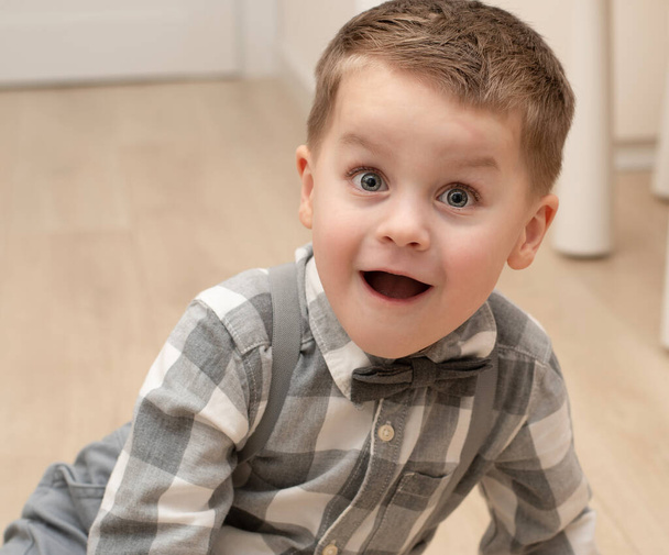 Emotionen der Überraschung und Freude auf dem Gesicht des Kindes. Ein kleiner gutaussehender Junge von 4 Jahren im Hemd mit Fliege zeigt eine Fratze mit einem Gesichtsausdruck. Nahaufnahme. Porträt - Foto, Bild
