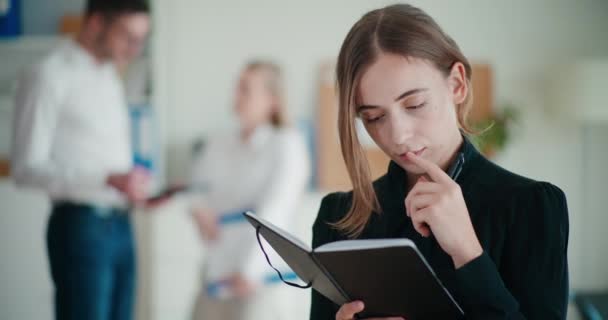 Jonge zakenvrouw schrijft strategie in dagboek terwijl collega 's bespreken tijdens vergadering op kantoor - Video