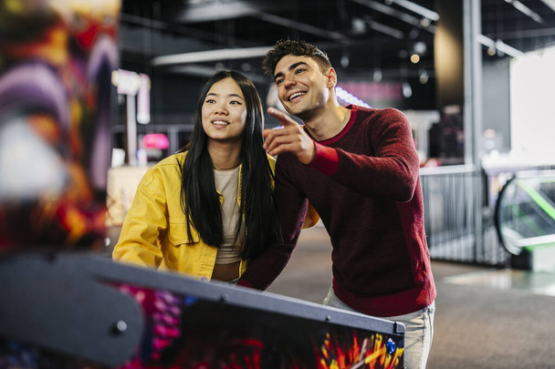 multiracial couple friends playing pinball in arcade amusement game room - Φωτογραφία, εικόνα