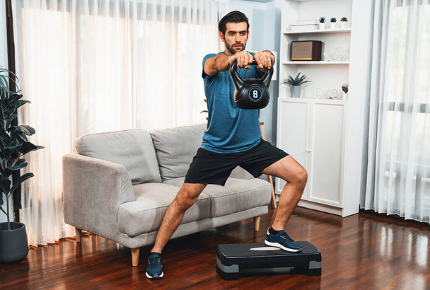Sportovní tělo a aktivní sportovní muž dělá dřepy s kettlebell hmotnost pro efektivní zacílení svalové zisky v veselosti doma jako koncept zdravého fit tělo domácí cvičení životní styl. - Fotografie, Obrázek