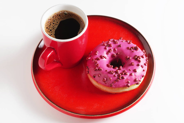 Donut rosa com bolas de açúcar e xícara de café em utensílios vermelhos no fundo branco - Foto, Imagem