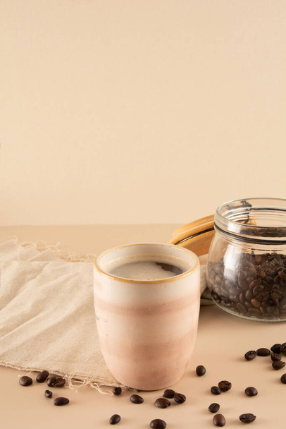 Кавовий кухоль на бежевому фоні з кавовими зернами та столовою тканиною спереду - Фото, зображення