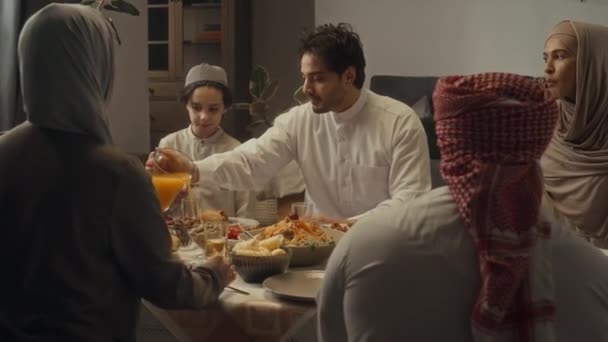 Hátsó felvételek nagy iszlám családról, akik együtt vacsoráznak otthon. A fiatalember narancslevet önt a poharakba és hozzátartozókat szolgál fel. - Felvétel, videó