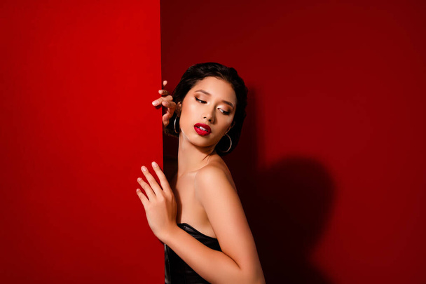 Φωτογραφία της ελκυστικής κινεζικής νεαρή γυναίκα εξετάσουμε κενό χώρο φορούν μαύρα δερμάτινα ρούχα που απομονώνονται σε κόκκινο χρώμα φόντο. - Φωτογραφία, εικόνα