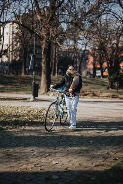 Una mujer en atuendo casual disfrutando de un paseo con su bicicleta retro en un parque urbano sereno, encarnando vibraciones de estilo de vida activo y pausado. - Foto, Imagen