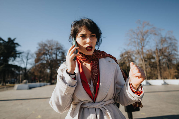 Una mujer de negocios musulmana comprometida con un abrigo de invierno que tiene una conversación importante en su teléfono al aire libre en un día soleado de invierno. - Foto, Imagen
