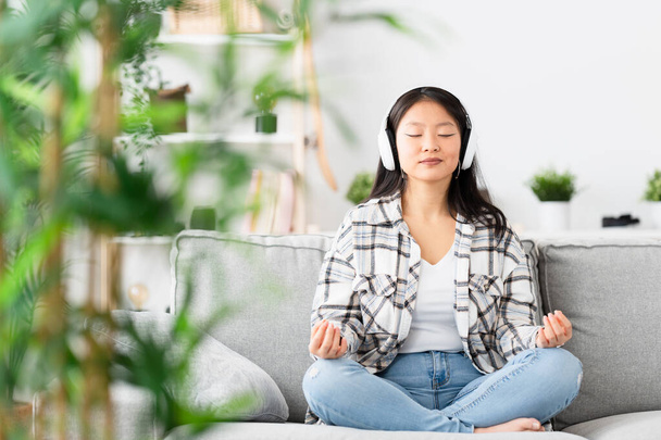 Cinese donna citando cuffie meditando da solo sul divano - Foto, immagini