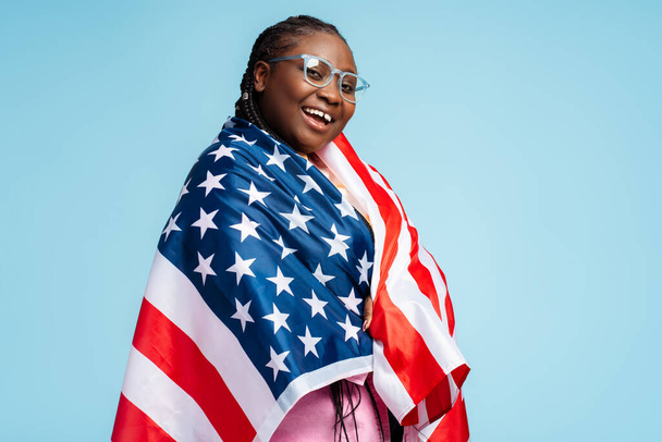 Πορτρέτο ευτυχισμένη όμορφη Αφροαμερικανή γυναίκα κρατώντας ΗΠΑ σημαία γιορτή Ημέρα Ανεξαρτησίας. 4 Ιουλίου, ελευθερία. Έξυπνος μαθητής φορώντας κομψά γυαλιά κοιτάζοντας την κάμερα, την έννοια της εκπαίδευσης - Φωτογραφία, εικόνα