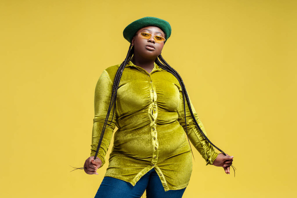 Portrait confident stylish African American woman wearing eyeglasses, beret, trendy dress isolated on background. Plus size fashion model posing for pictures in studio. Body positive, individuality - Photo, Image