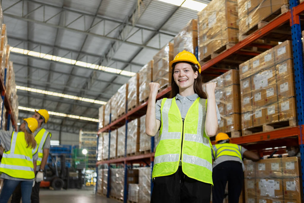 Femme heureuse montrent la main portant l'uniforme de sécurité regardant la caméra debout dans l'usine d'entrepôt. stock de travailleuses professionnelles inspectant les marchandises sur les étagères dans l'entrepôt. - Photo, image