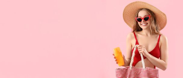 美しい若い女性はビーチバッグとテキスト用のスペースを持つピンクの背景に日焼け止めクリームを保持しています - 写真・画像