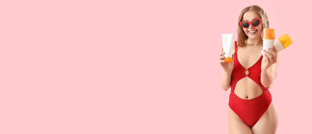 Красивая молодая женщина в купальнике держит кремы от загара на розовом фоне с пространством для текста - Фото, изображение
