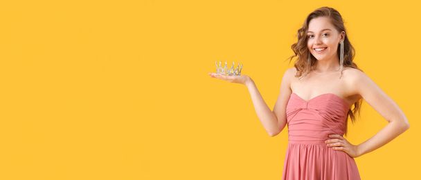 gelukkig jong meisje in prom jurk houden tiara op gele achtergrond met ruimte voor tekst - Foto, afbeelding
