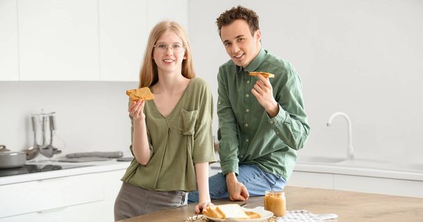Happy young couple with tasty nut butter toasts in kitchen - Photo, Image