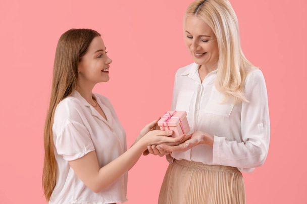 Junge Frau begrüßt ihre Mutter mit Geschenk auf rosa Hintergrund - Foto, Bild