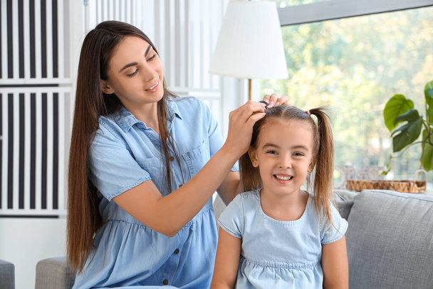Happy mother tying daughter's ponytails in living room - Photo, Image