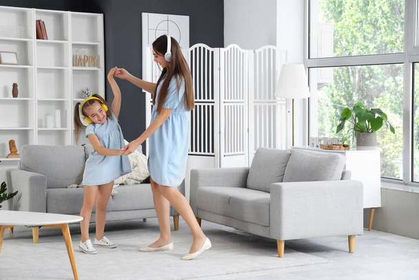 Šťastná matka se svou dcerou ve sluchátkách tančí v obývacím pokoji - Fotografie, Obrázek