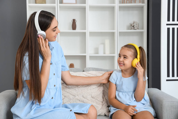 Happy mother with her little daughter in headphones sitting on sofa at living room - Photo, Image