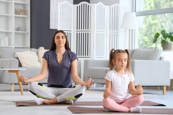Glückliche Mutter mit ihrer kleinen Tochter beim Meditieren auf dem Fußboden im Wohnzimmer - Foto, Bild