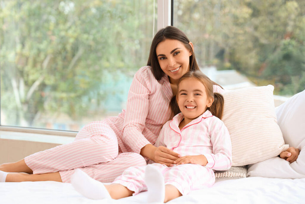 Glückliche Mutter mit ihrer kleinen Tochter im Pyjama, die Zeit zusammen auf dem Bett verbringt - Foto, Bild