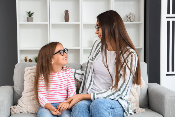 Happy mother with her little daughter in eyeglasses sitting on sofa - Photo, Image