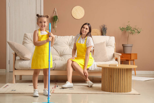 Madre feliz con su hijita en delantales limpiando la sala de estar juntos - Foto, imagen