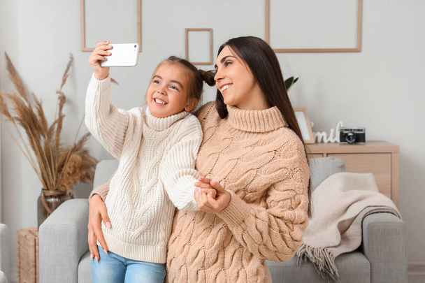 Glückliche Mutter mit ihrer süßen kleinen Tochter beim Selfie im Wohnzimmer - Foto, Bild