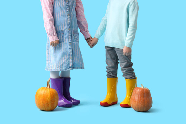 Petits enfants en bottes en caoutchouc avec citrouilles sur fond bleu - Photo, image