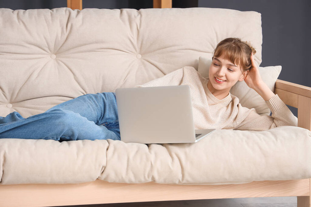 Giovane donna che utilizza il computer portatile sul divano a casa
 - Foto, immagini