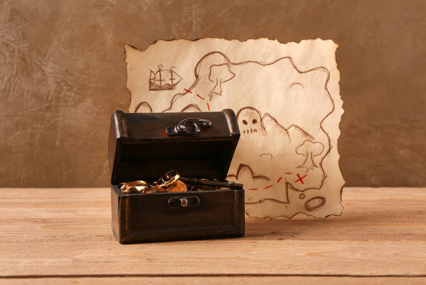 Παλιό μπαούλο με θησαυρούς, πυξίδα και χάρτη σε ξύλινο τραπέζι κοντά σε καφέ τοίχο - Φωτογραφία, εικόνα