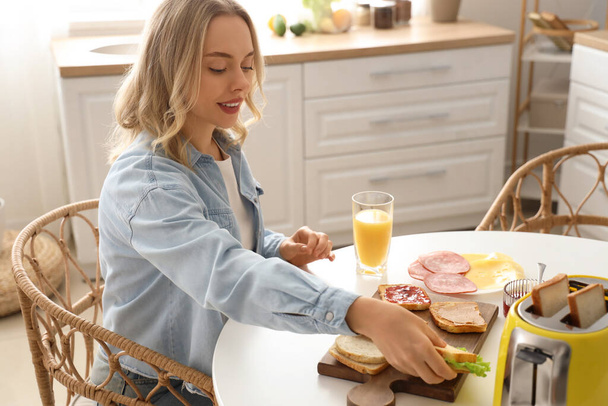 Junge schöne Frau isst leckeres Sandwich in der Küche - Foto, Bild