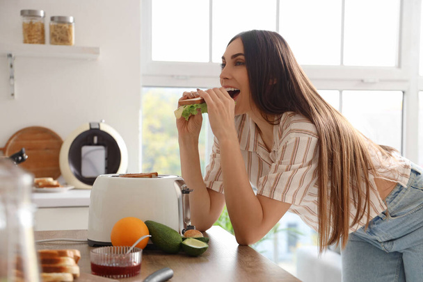 Giovane bella donna felice mangiare gustoso panino in cucina - Foto, immagini